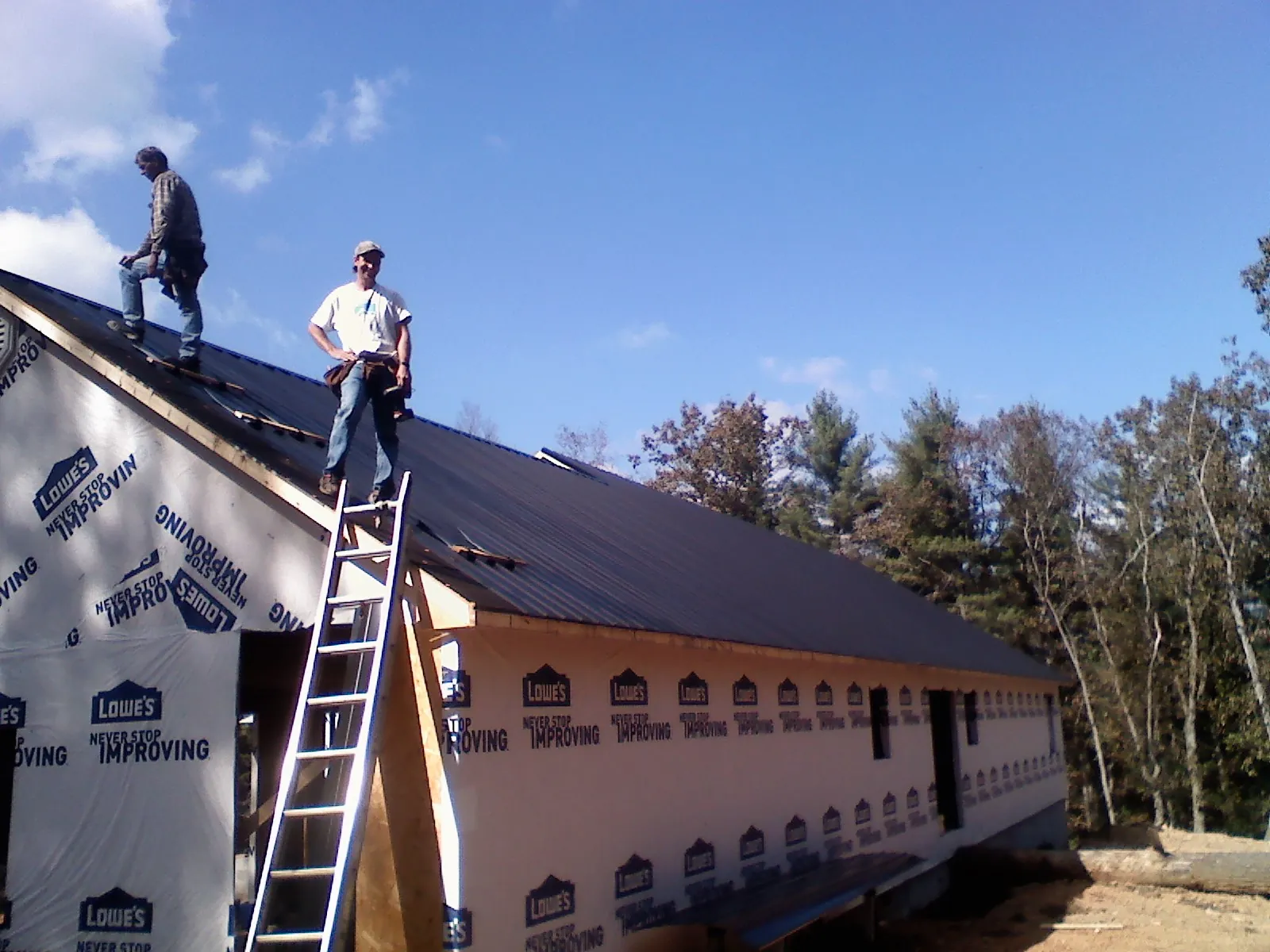 Two roofers standing on a long dark metal roof over a wrapped building in Wilmot