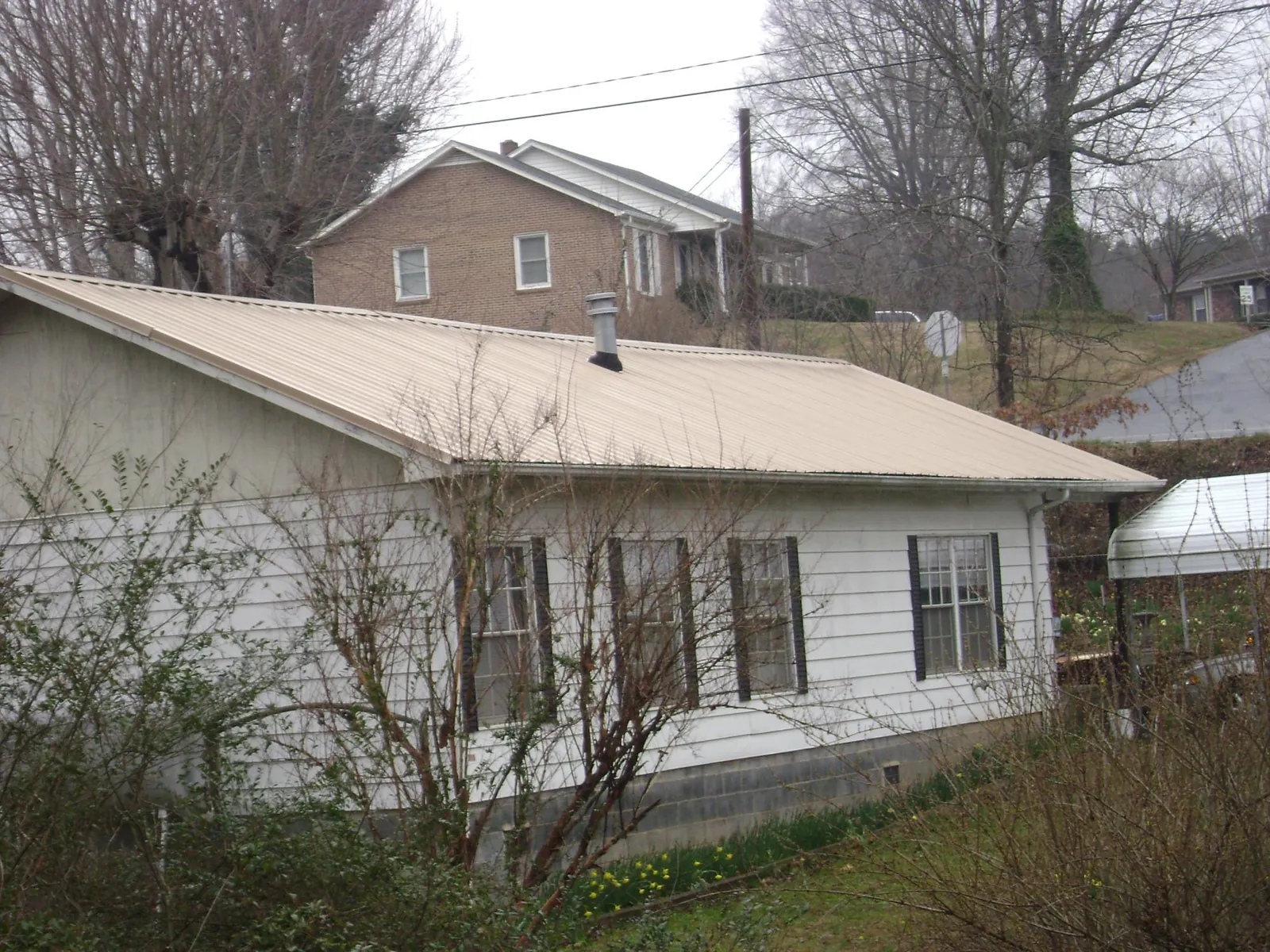 Tan metal roof on a white sided house set into a hillside — Commercial Roofing by Roofing Brothers in Wilmot