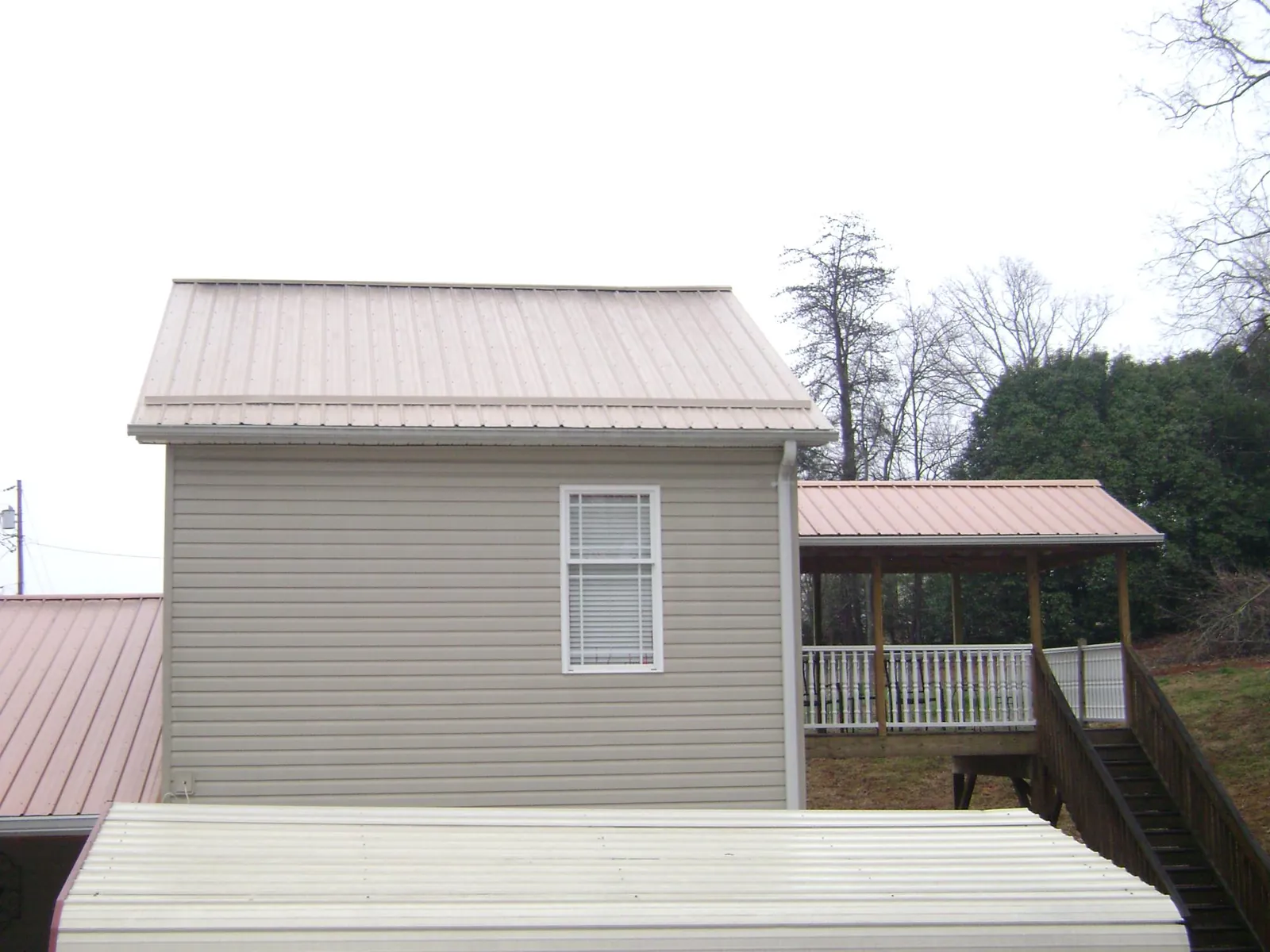 Tan metal roofs on a two story addition and attached porch, from a Roof Replacement job in Wilmot